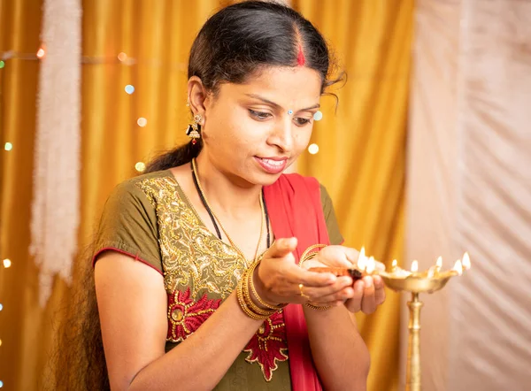 Happy smiling Indian woman lighting lantern or Diya Lamp during festival ceremony at home - concept of traditional festival and ritual celebrations. — Stock Photo, Image