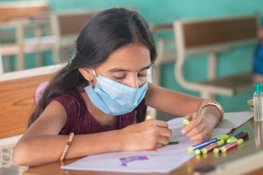 Tıp maskeli genç kız, Coronavirus ya da covid-19 salgınından dolayı okulda güvenlik önlemleri kavramı üzerine çizim yapmakla meşgul..