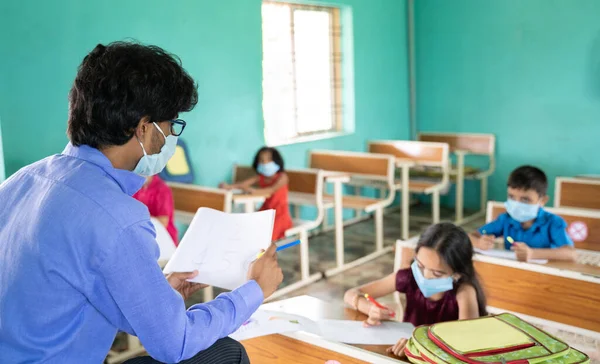 Teacher in medical mask with limited kids teaching at classroom while maintaining social distance due to coronavirus or covid-19 pandemic — Stock Photo, Image