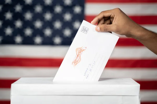 Maski, India 14 september, 2020: Begreppet Mail i omröstningen i USA val - händer släppa post i valurnan med oss flagga som bakgrund. — Stockfoto