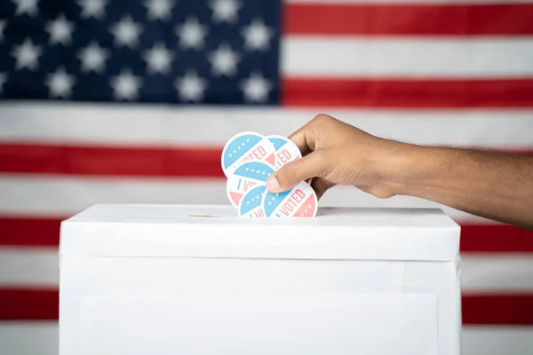 Close up of Hands dropping multiple I Voted sticker inside Ballot box with US flag as background, Concept of fraud in USA elections. — Stock Photo, Image