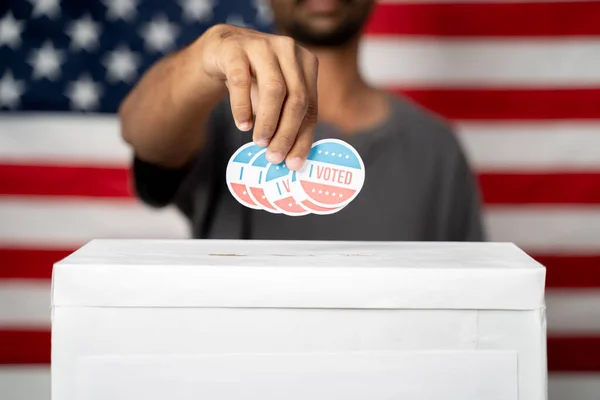 Närbild av händer släppa flera I Röstade klistermärke inuti valurna med USA flagga som bakgrund, Begreppet bedrägeri i USA val. — Stockfoto