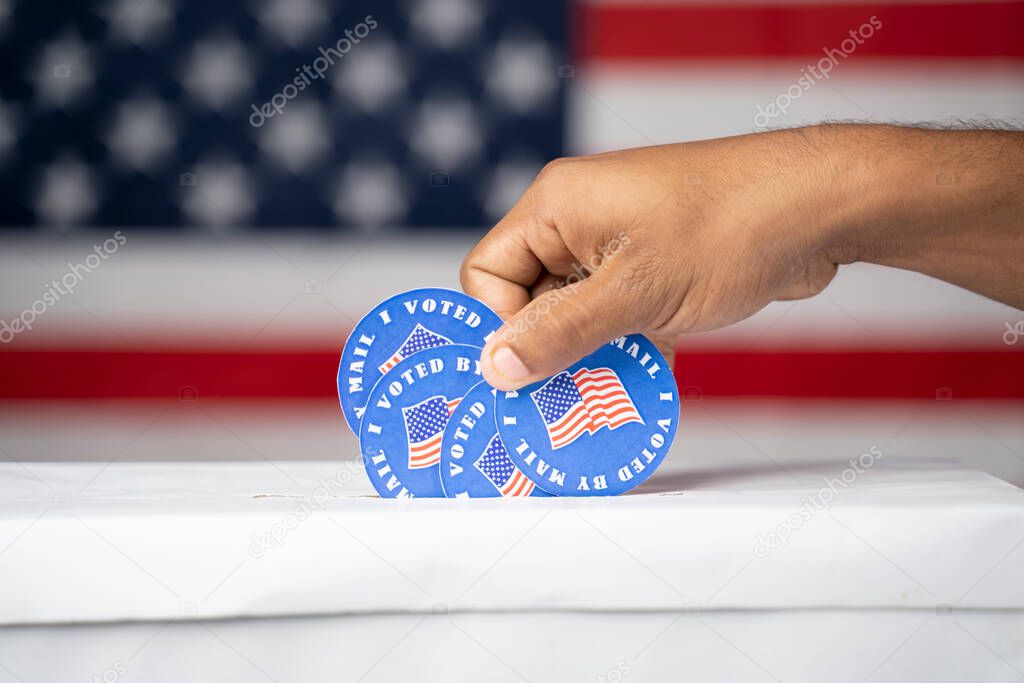 Close up of hands putting multiple I voted my Mail stickers inside the box with US flag as background - Concept of Vote by mail fraud in USA elections