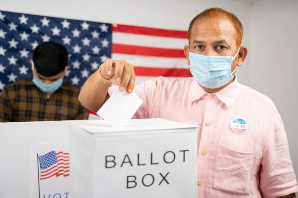 Людина в медичній масці поміщає бюлетені в бланк для голосування, дивлячись на камеру - Концепція голосування людини і людей, зайнятих у опитуванні кабінки на виборах США. — стокове фото
