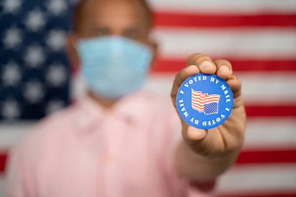 Homem de máscara médica mostrando Eu votei por adesivo de correio com bandeira dos EUA como fundo Conceito de correio na votação nas eleições dos EUA. — Fotografia de Stock