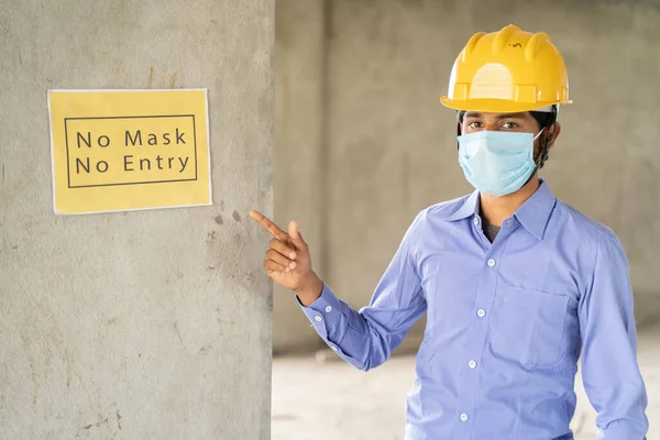 Работник, указывающий на отсутствие маски Нет Входные вывески на стене на рабочей строительной площадке, чтобы защитить от коронавируса или ковид-19 на рабочих местах - концепция здоровья и безопасности труда во время пандемии — стоковое фото