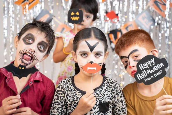 Grupa dzieci w kostiumach Halloween co gestykulacyjne straszne lub straszne twarze trzymając pędy stoiska na dekorowanym tle patrząc w aparat. — Zdjęcie stockowe
