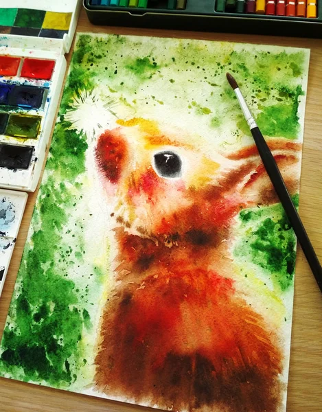 Bright colorful rabbit illustration on green background, painted by hand with watercolor. Vertical format, next to the illustration there are paints and a brush of squirrel.
