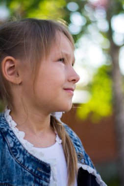 Kot ceketli ve beyaz elbiseli bir kız gün batımında parkta yürüyor.