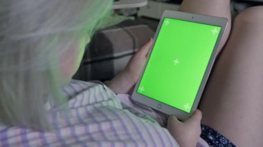 Genç kadın el ile yeşil perde, lieng Divan evde tablet kullanma. Arkadan görüntüleyin. Chroma anahtar.