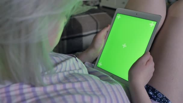 年轻女子双手用平板电脑与绿色屏幕 亮在沙发上在家里 从后面看 色度键 — 图库视频影像