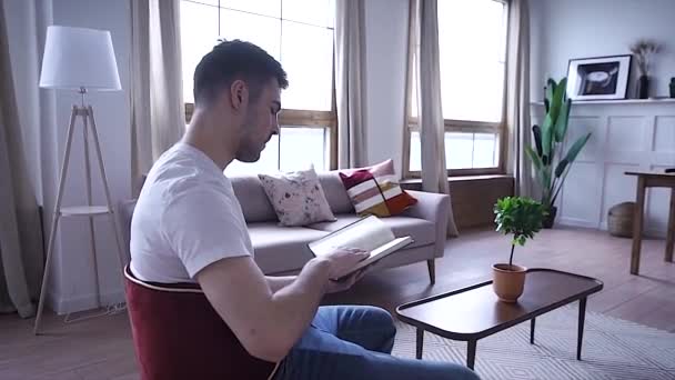 Unga Allvarlig Man Läser Bok Som Sitter Stol — Stockvideo