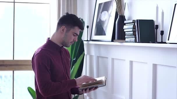 Красивий Молодий Чоловік Читає Книгу Вдома Своїй Вітальні Стоячи — стокове відео