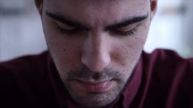 Portre ciddi genç adam kim aşağı bakmak ve sonra oturma odası arka plan üzerinde fotoğraf makinesinde arıyorum. Yakın çekim.