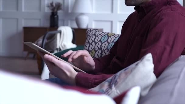 デジタル タブレットの緑色の画面表示に触れるソファに座ってリラックスした若い男 — ストック動画