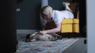 Genç bir kadın köpeğini sandalyede otururken okşadı. Yerde uyuyan sevimli köpek yavrusu. Aşk ve özen sahnesi.