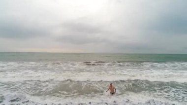 Hava görüntüsü - hipster adadaki sahilden geliyor. Atlantik Okyanusu ve siyah kum. Adam okyanustan çıkıyor.