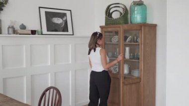 Günlük giysiler giyen genç beyaz bir kadının yemek masasına dört beyaz tabak koyması.