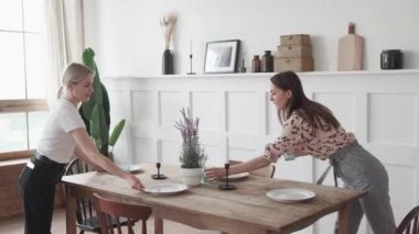 Mutfakta duran üç kız gülümsüyor ve ortak bir akşam yemeği için tabaklar hazırlıyorlar.