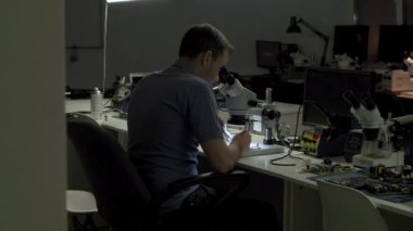 Elektronik mühendisi karanlık bir ofiste ekranı olan bir elektrik kartına işlemci lehimliyor.