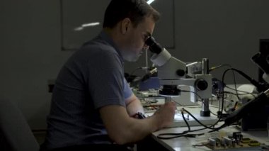 Elektronik mühendisi karanlık bir ofiste ekranı olan bir elektrik kartına işlemci lehimliyor.