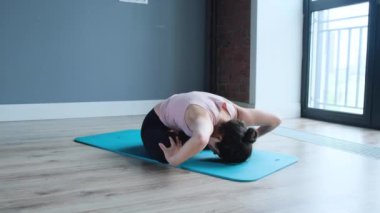 Evde yoga yapan genç Hintli kadın. Genç bir bayan sporcunun mavi bir mindere uymak için evdeki yoga pozisyonunu sergilediği yakın çekim.
