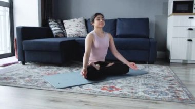 Yoga lotusu pozu veren meditasyon yapan kadın. Evde yoga yapan genç Hintli kadın. Genç bir bayan sporcunun, formda olmak için mavi bir paspasın üzerinde yoga yaparken çekilmiş yakın plan fotoğrafı.