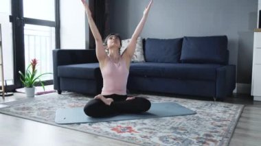 Evde mavi yoga minderinde spor kıyafetleriyle yoga yapan çekici bir kadın..