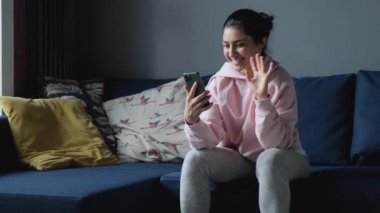 Akıllı telefonu elinde tutan ve akıllı telefonu koltukta otururken kullanan bir kadın. Neşeli kadın elinde akıllı telefon tutuyor ve internetten video görüşmesi yapıyor. 