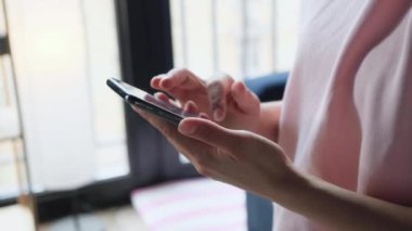 Yan görüş. Evdeki oturma odasında akıllı telefon kullanan ve mesaj yazan bir kız. Genç kadınların yakın plan fotoğrafları.