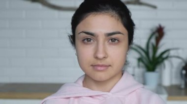 Parlak bir odada duran ve kameraya bakan genç bir Hintli kadının yakın plan fotoğrafı.