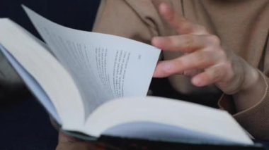Bir kadının elini kapayarak kitap okuyor ve sayfayı çeviriyor.