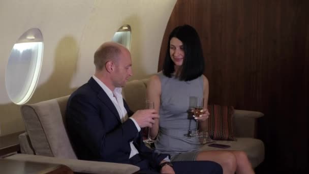 ソファパーソナルビジネスジェットプレーンに座ってシャンパンを飲む笑顔若いカップルの男の終わります — ストック動画