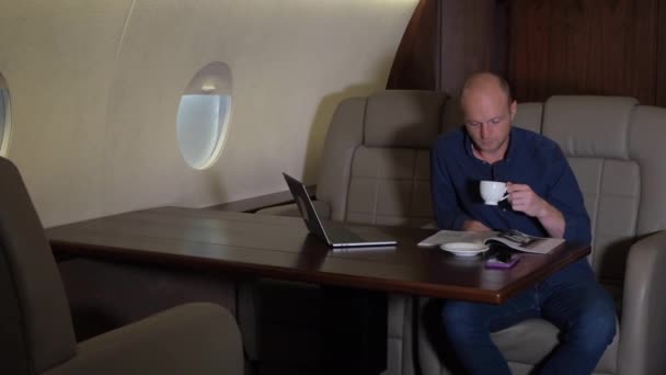 若いビジネスマンはコーヒーを飲み 雑誌を読む 彼は彼のビジネスジェットに座っている 男性チーフ銀行家取締役ブローカーの肖像民間航空機での取引を神経質な観察 — ストック動画