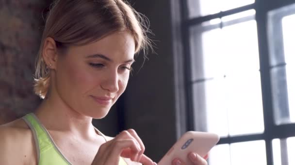 Μια Νεαρή Ξανθιά Γυναίκα Χρησιμοποιεί Ένα Smartphone Ρολόγια Ένα Σχέδιο — Αρχείο Βίντεο