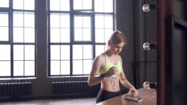 Genç bir sarışın kadın spor salonuna ara veriyor. Su, mesajları kontrol ediyor ve akıllı telefonuyla büyük pencereli bir spor salonunda egzersiz programı yapıyor.