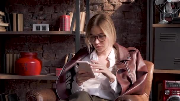 一个年轻的女商人在一间明亮的大办公室里用智能手机坐在椅子上 — 图库视频影像
