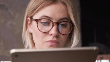 Moda gözlüklü genç sarışın kadını yakından takip et, internette sörf yap. Şık Sarışın, evinde bilgisayarla ya da Tablet 'le çalışıyor. Monitör ekranı gözlüklere yansıyor