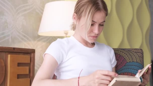 Joven Mujer Rubia Leyendo Libro Que Está Sentada Una Silla — Vídeo de stock