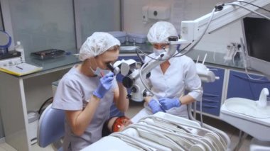 Bir kadın uzman diş tedavisi yapıyor. Mikroskobu kullanıyor. Endodontist kanalları tedavi ediyor..