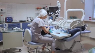 Genç bir kadın diş hekimi ve asistan ameliyata hazırlanıyor. Muayeneye göre hastanın dişlerine koruyucu bir bant takılmış.