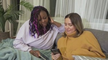 Afro-Amerikan ve Avrupalı Farklı Milletlerden Genç Tarz Kadınları Akıllı Telefon İletişiminde Fotoğraflara Bakın, Evde Kalın, Akşam, Gülümseyin, Konforlu Daire