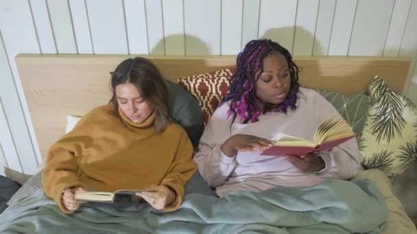 アフリカ系アメリカ人と白人女性の肖像 読書本の上に横たわる 夜の居心地の良いアパート Ulybayutsya笑い研究を読む — ストック動画