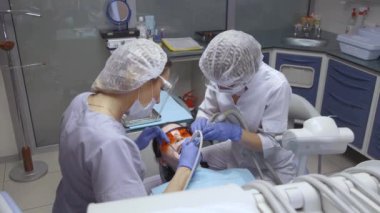 Gözlüklü iki genç kadın hastayla diş temizliği yapıyor ve hastayı muayene ediyor, beyaz önlük ve maske takıyor.