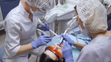 Bir dişçinin ve asistanının sinematik görüntüleri ofisteki hastanın ağzını inceliyor. Diş matkabı, sondaj makinesi, dişçinin elindeki profesyonel aletler. Diş sağlığı konsepti kopyalama alanı