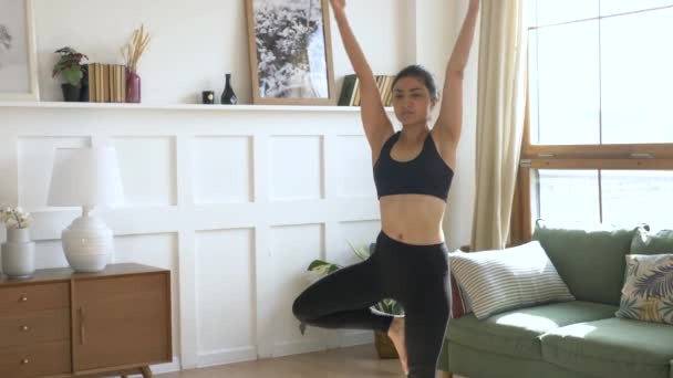 若いインド人女性瞑想カーペットと手の上に立って名前カメラを見てヨガをやってバランス運動をする ブラックスポーツウェアライトルーム朝の自宅で — ストック動画