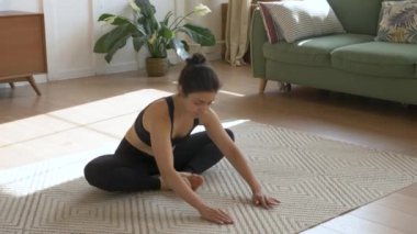 Genç Hintli kadın, gülümseyen meditasyon yapıyor, halının üzerinde oturuyor ve esniyor, yoga yapıyor, siyah spor giyinme odası sabahları evde.
