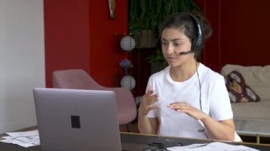 Genç Hintli öğrenci online ders izliyor ve evden ders çalışıyor. Genç bir kadın video ekranında bilgisayar ekranına bakarken not alıyor. Kız öğrenci evden ders çalışıyor.