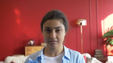 Silikon eldivenli genç bir Hintli kadının yakın plan portresi tıbbi maske takıyor, kameraya bakıyor, apartmandaki parlak ve samimi odaya bakıyor.