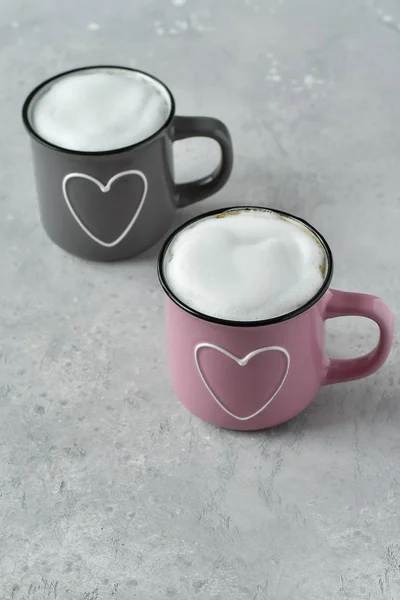 pink and gray cups with cappuccino. cups with  hearts, gray background. concept of romantic love, romantic breakfast, concept of romantic couple.  selective focus and copy space